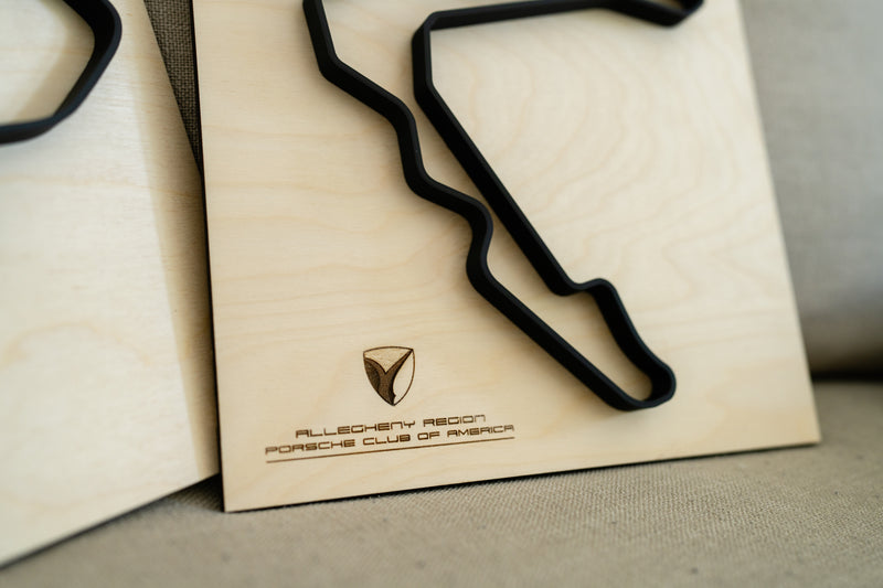 A closer up photo of the Allegheny Region Porsche Club of America logo. The wood framed race track is resting on a beige sofa.